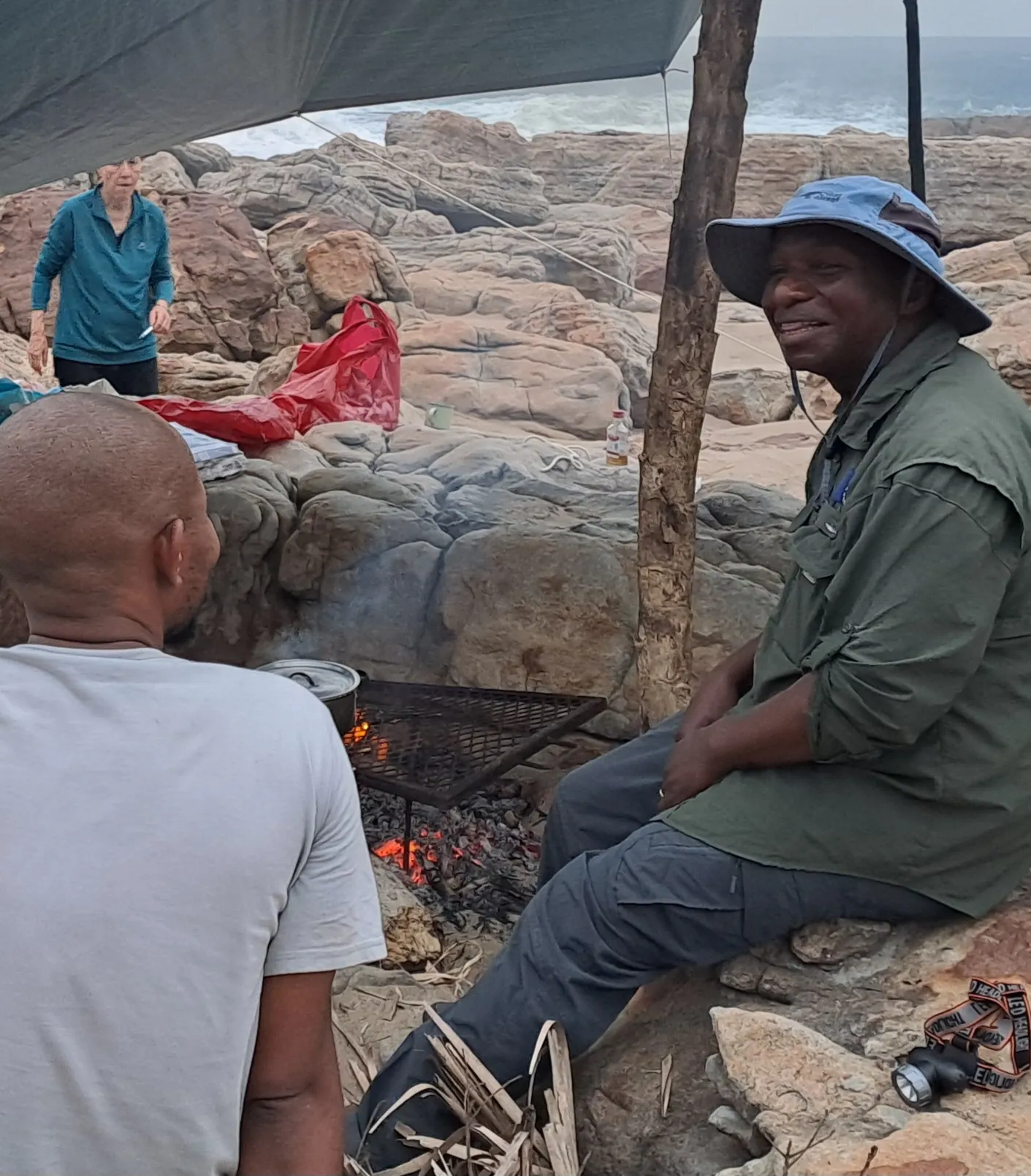 Campfire cooking under tarp by rocky coastline with ocean view