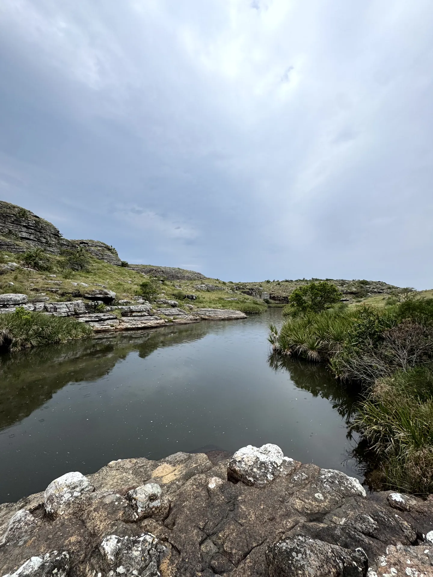 Calm river flowing between rocky vegetated hills under cloudy sky