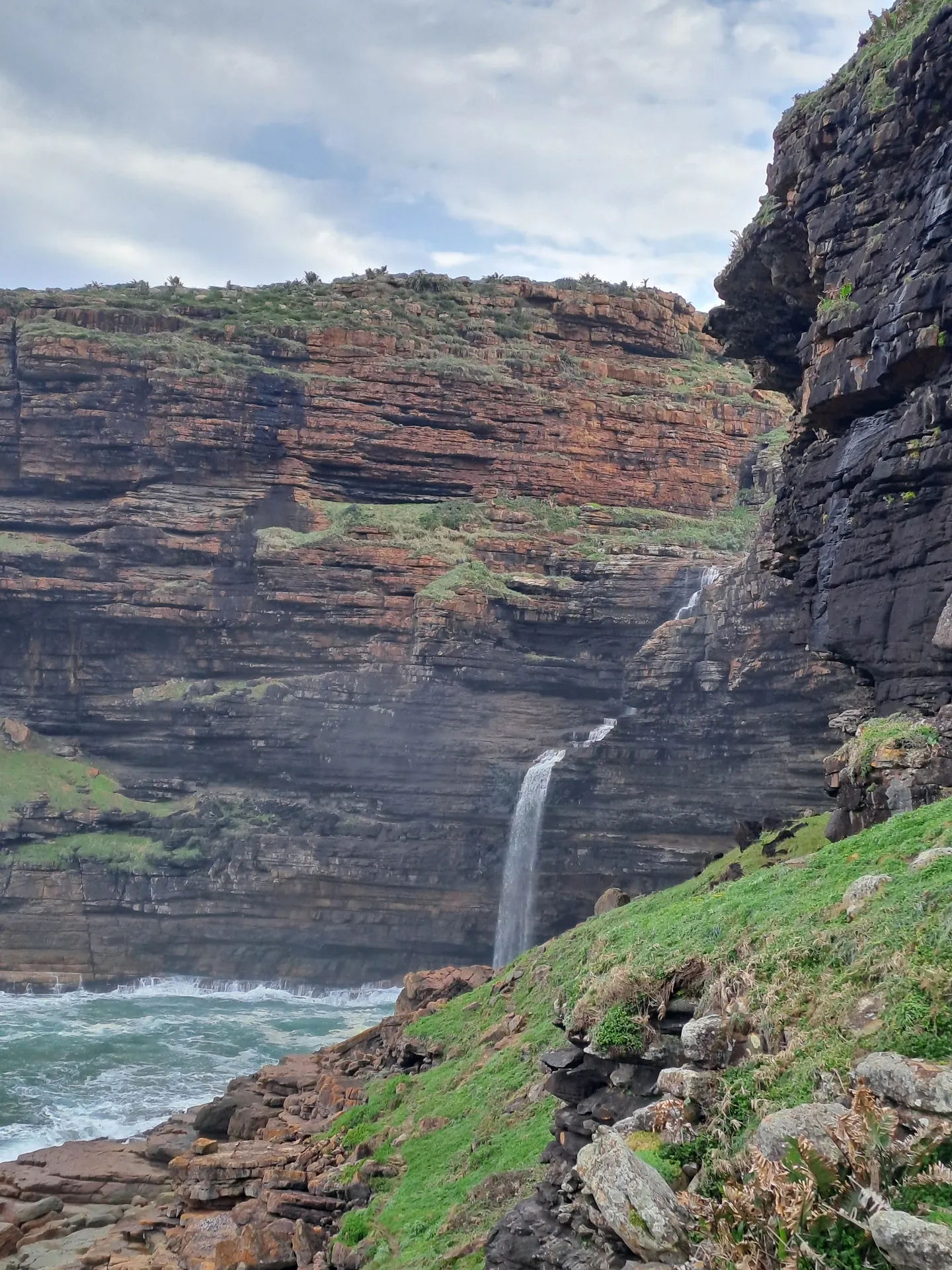 Dramatic waterfall cascading down layered cliff into ocean